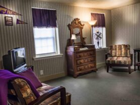 room with dresser, tv, chairs, striped wallpaper