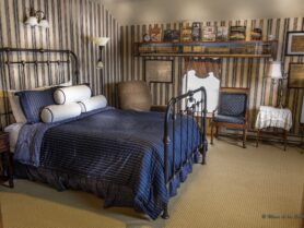 bedroom with iron bed with blue bedspread, 2 chairs