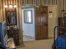 iron bed with blue bedspread, looking into bathroom