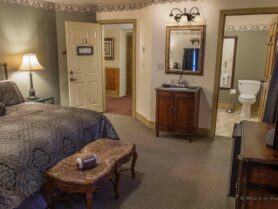 bed with brown bedspread, lamp, bench with football looking into bathroom